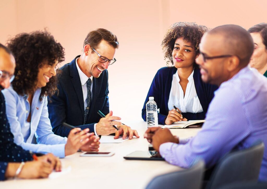 Groupe de managers en réunion, échange convivial et décontracté autour d’une table, avec notes et bouteille d’eau. communication non violente en management est présentée comme méthode.