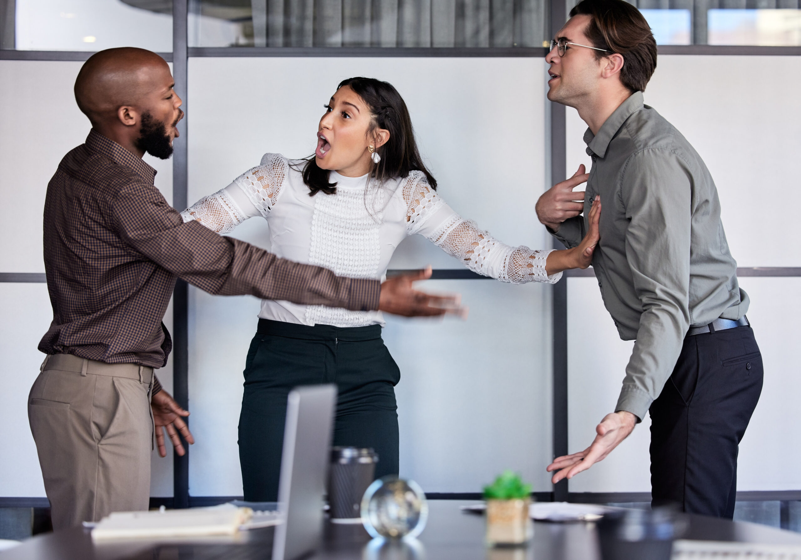 Trois collègues en désaccord au bureau, tensions visibles et gestes d’assertion; un cadre pour apprendre comment désamorcer un conflit au travail.
